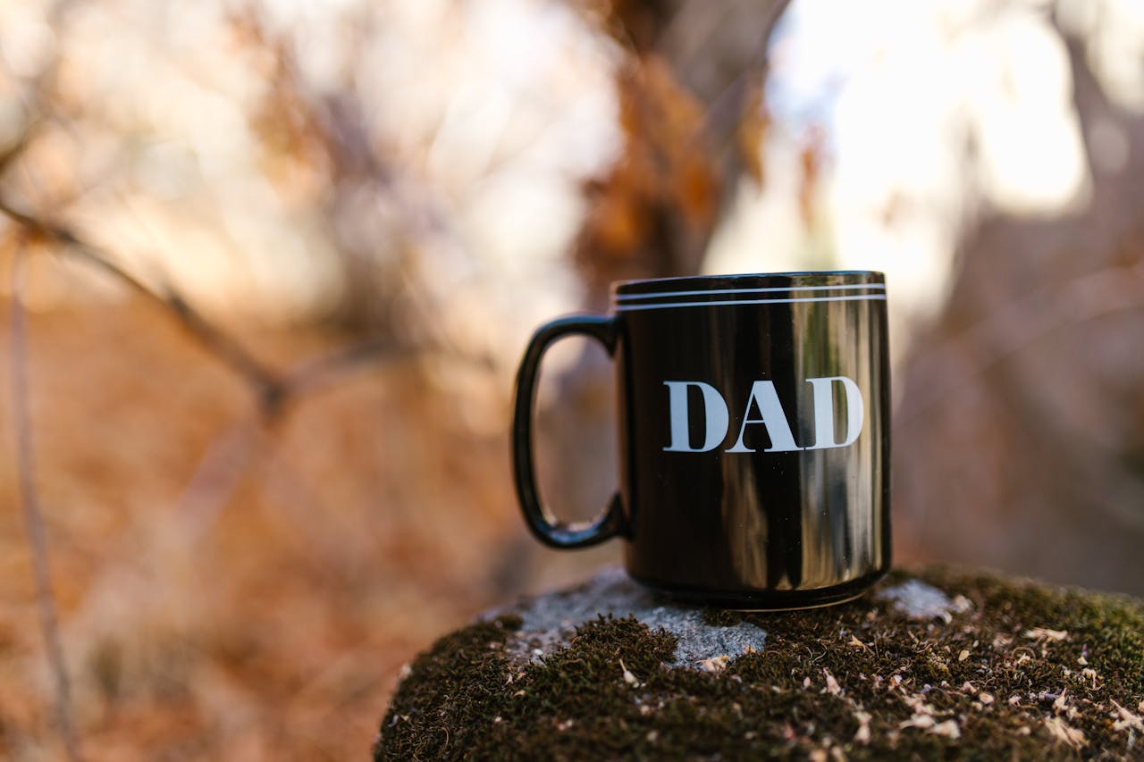 Close-up of a ceramic mug with 'Dad' text on a mossy rock outdoors, ideal for Father's Day.